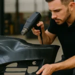 Technician heating and inspecting a removed plastic bumper to reshape a dent without using tools