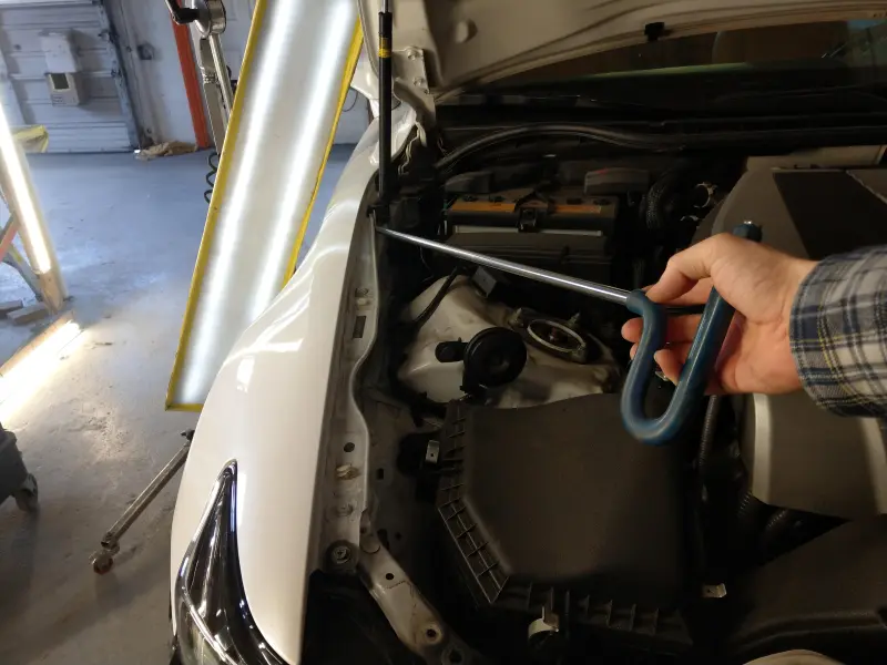 Dent removal tool in action during a paintless dent repair spotlight, showing precise tool movement used to release tension and restore the panel.