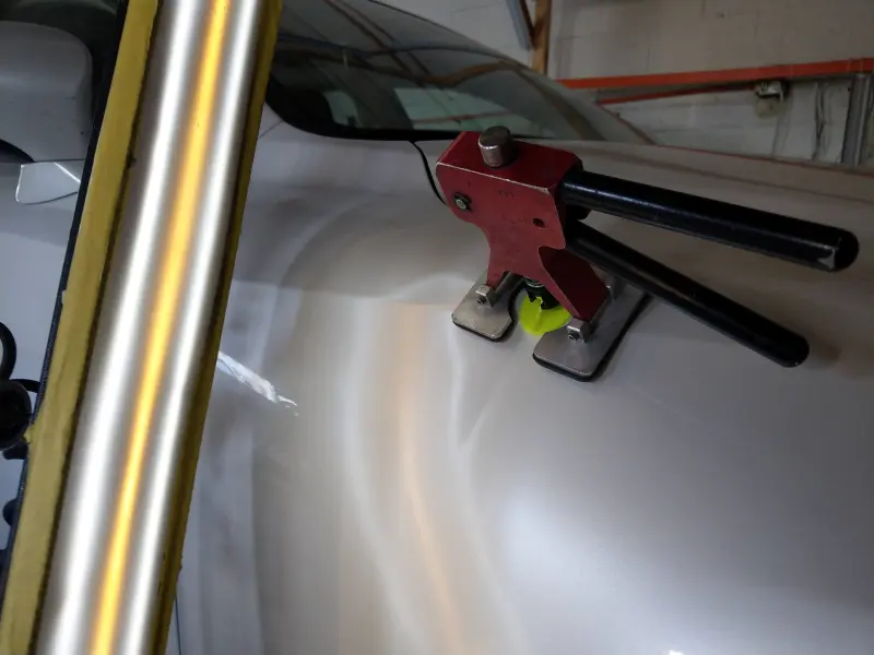 Glue pulling device prepared for use during a paintless dent repair spotlight, showing the setup before pulling the dent.