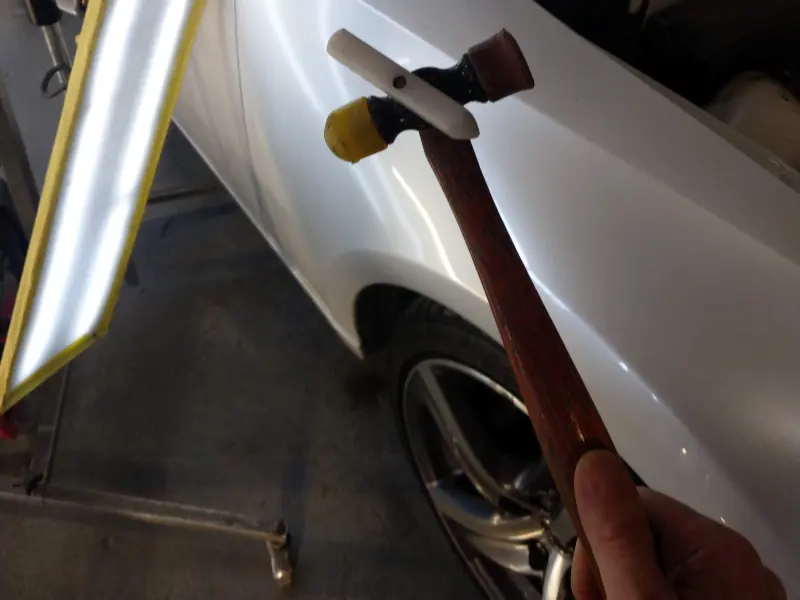 Tap‑down tool and hammer used during a paintless dent repair spotlight, showing the controlled tapping process used to refine the panel.